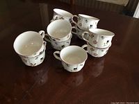 Stacked arrangement of 11 white porcelain tea cups with colorful floral patterns and gold rim and handle accents from Villeroy & Boch Petite Fleur series