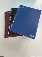 Three wire bound notebooks with poly covers in blue, black, and maroon, labeled 'Wired'
