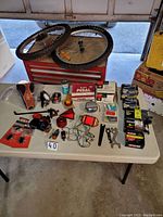 Full table view showing two bicycle wheels, multiple boxed and loose bike parts including brake pads, pedals, lights, wrenches, and tubes.