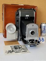 Full view of camera extended with leather case, Wink Light flashlight, user manual, and Pepsi can for scale