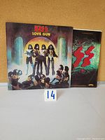 Front cover of KISS Love Gun vinyl LP showing band in makeup and costume with figures kneeling below them, and original inner sleeve next to it.