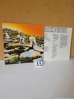 Front gatefold vinyl album cover with image of nude children climbing rock formations under an orange sky, with lyric insert behind.
