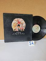 Front cover of Queen's 'A Day at the Races' vinyl LP showing the band's crest design. Vinyl record partially visible to the right.