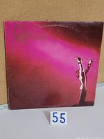 Front cover of Queen vinyl LP showing artwork with figure holding pin and text with wear on sleeve edges.