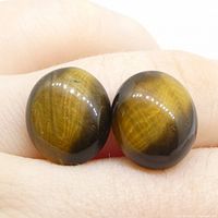 Pair of polished oval cabochon Tiger's Eye quartz gemstones shown on human fingers, displaying brown and golden yellow colors with chatoyant effect.