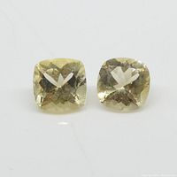 Two yellow heliodor gemstones displayed together showing their square cushion shape and faceted cut under direct light.
