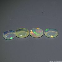Four oval white opal gemstones aligned horizontally showing play-of-color on a dark surface.