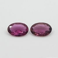 Two oval-shaped, faceted pink tourmaline gemstones shown on white background to detail shape, size, and color.