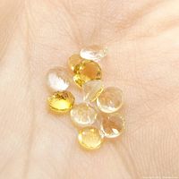 Photo of 10 small round cut citrine gemstones in hand showing size, color, and clarity.