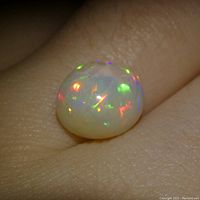 Close-up showing opal with brilliant play-of-color on hand background.