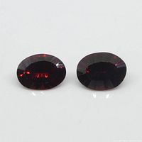 Close-up photo of two oval deep red almandine garnet gemstones on white background.