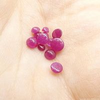 Twelve pink to red round cabochon rubies displayed on a palm, showing glossy domed surfaces and size variation.