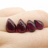 Four pear cabochon cut purplish-red rhodolite garnet gemstones displayed on a hand, showing their size and shape.