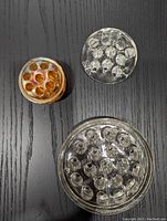 Top view of three floral frogs on dark surface showing clear glass and marigold carnival glass surfaces with multiple holes for flower stems.