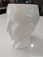 Side profile view showing geometric head planter with smooth white glaze and minor surface marks.