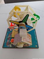 Top angled view of the Ferris wheel toy showing the multi-colored seats and base with game board print