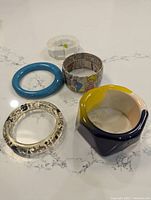 Top view of five bracelets arranged on a white marble surface showing varied styles and colors