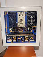 Full view of the framed colorful peasant painting depicting village life with large patterned fabrics overhead and figures in traditional attire in deep blue, yellow, and purple colors.