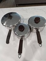 Three stainless steel pots with lids, two smaller Lagostina pots with dark handles and lids, and one larger Kenmore pot.