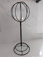 Full view of black metal hat rack with spherical wireframe top and circular base against a white countertop background