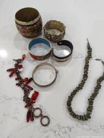 Photo showing six bracelets and a green stone necklace on a marble surface.