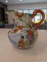 Front-side photo showing detailed painted figures of male in traditional dress and child with female, ornate handle with raised gold design