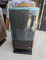 Front view of one speaker wrapped in plastic on black stand