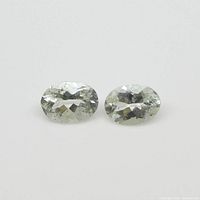 Two oval faceted blue-green beryl gemstones shown on white background.