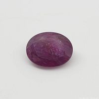 Close-up of oval faceted pink-red ruby gemstone on white background.