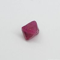 Photo of rough octahedron pink Jedi Spinel gemstone on white background showing shape and color.