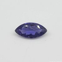 Close-up image of a marquise-shaped violet-blue Iolite gemstone on a white background, showing facets and clarity.