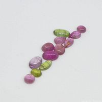 Twelve assorted pink and green tourmaline cabochon gemstones arranged in a group showing variety of shapes and colors