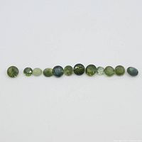 Twelve round green to blue sapphires laid out in a row, showing size and color variation.