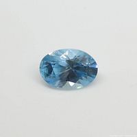 Close-up photo of oval blue zircon gemstone against white background showing cut and facets.