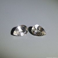 Two pear-shaped champagne morganite gemstones displayed side by side on a flat surface.
