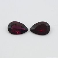 Two pear-shaped deep red Almandine Garnet gemstones on white background showing color and cut.
