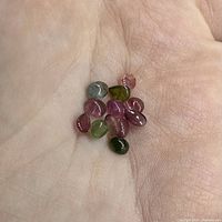 Top view of twelve small polished cabochon tourmaline stones in assorted colors held in palm of hand showing size and shape variety.