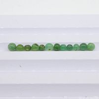 Twelve small polished spherical green emerald gemstones arranged in a row on a white surface for size and color comparison.
