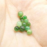 Close-up photo of 12 small spherical green emerald gemstones in the palm of a hand showing their size and color variation.