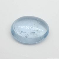 Oval cabochon cut blue aquamarine gemstone photographed from side view showing smooth polished surface and internal inclusions.