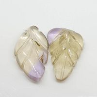 Two leaf-shaped carved ametrine gemstones, purple and yellow colors, side by side on a white surface.
