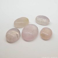 Five oval cabochon rose quartz gemstones on white background showing pink color and varying sizes.