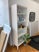 Full view of white bookshelf with five shelves, some decorative items on shelves, located indoors near a wall and clock.