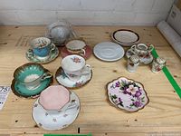 Photo showing five tea cups with matching saucers on wooden surface, plus three additional saucers and salt and pepper shakers with sugar container