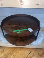 Full image of the round two-tier coffee table with dark wood top, showing metal frame and lower shelf.