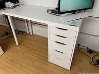 Full view of white Ikea desk with laminate wood top, four cylindrical metal legs on left, and attached five-drawer storage unit on right.