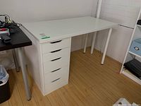 Front left angled view of the Ikea white laminate desk showing drawer unit and part of the white legs.