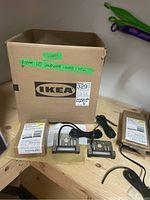 Cardboard box labeled IKEA containing approximately ten Kichler landscape lights, some in original packaging, displayed on wooden surface.