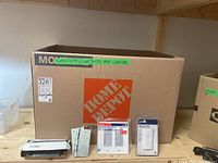 Box with label indicating contents: switches, plates, light bulbs, hinges, lighting, and visible items on shelf including wall plates, dimmer switch, and hinges.