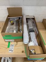 Boxed components of two Kichler wall mount light fixtures, items wrapped in plastic for protection